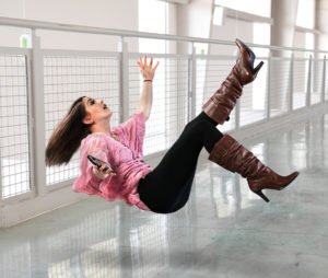 Una joven empresaria cayendo en el suelo dentro de un edificio de oficinas mientras sostiene un teléfono