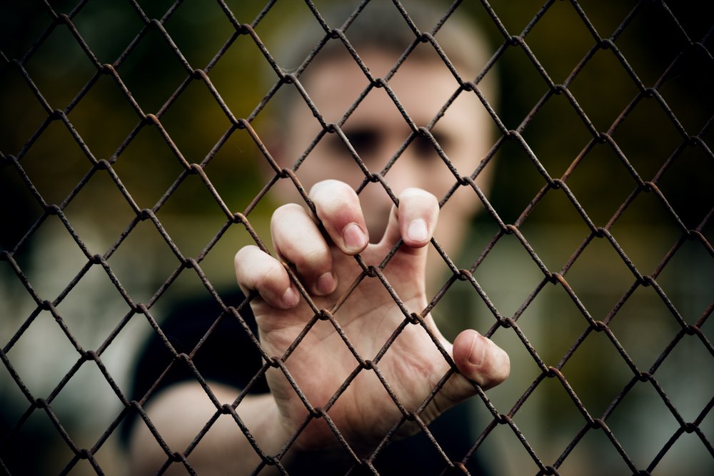 Young man holding onto a chain linked fence.