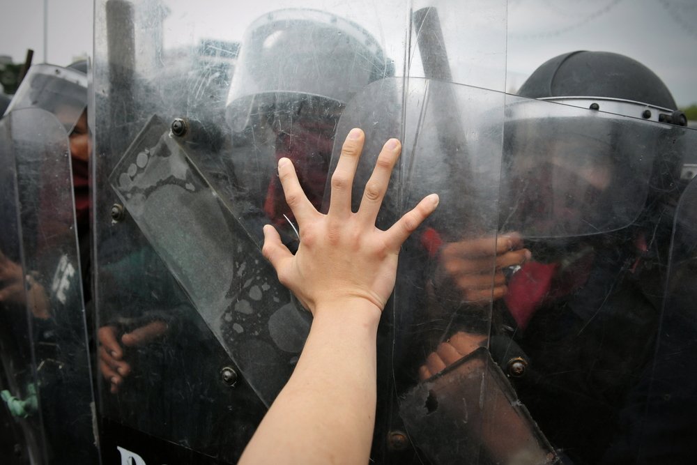 Rioter putting hand on police shield - battery on a peace officer is a crime in California per Penal Code 243c2 PC