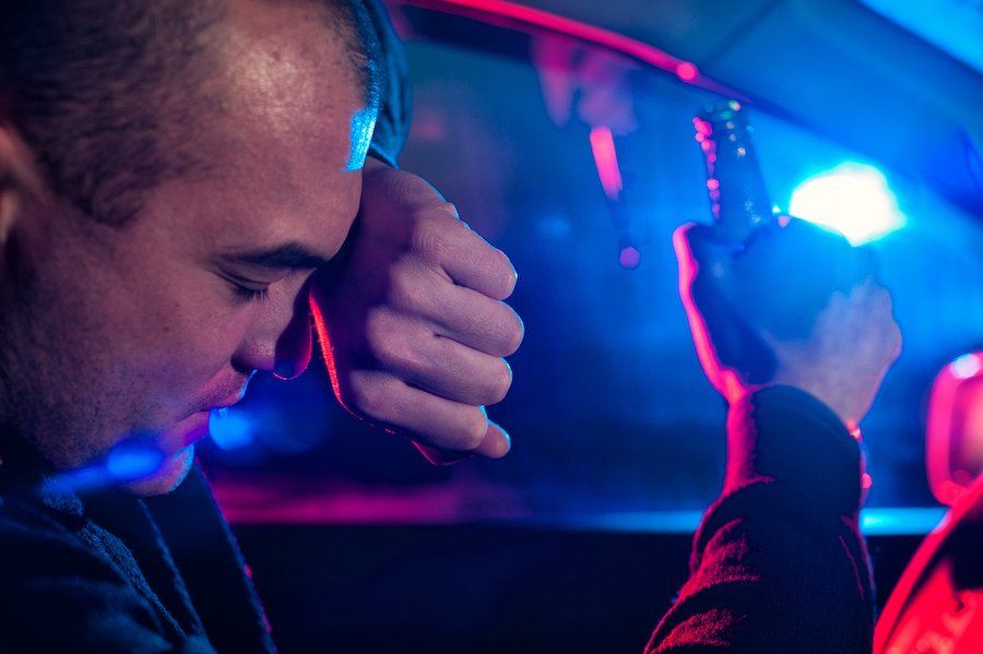 Hombre detrás del volante de un coche sosteniendo una cerveza después de ser detenido por la policía