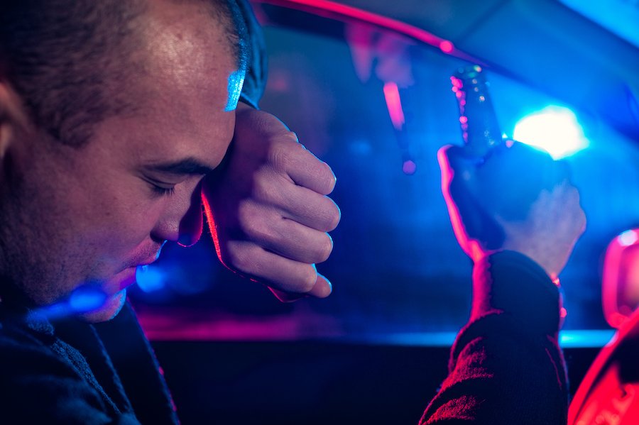 Man behind the wheel of a car holding a beer after being pulled over by police