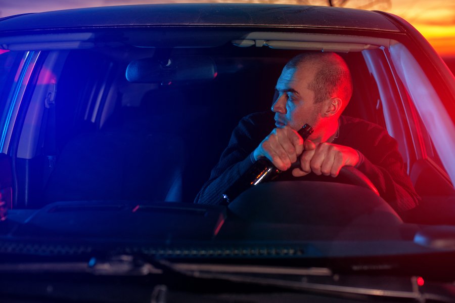 Man driving while holding beer with police lights behind him