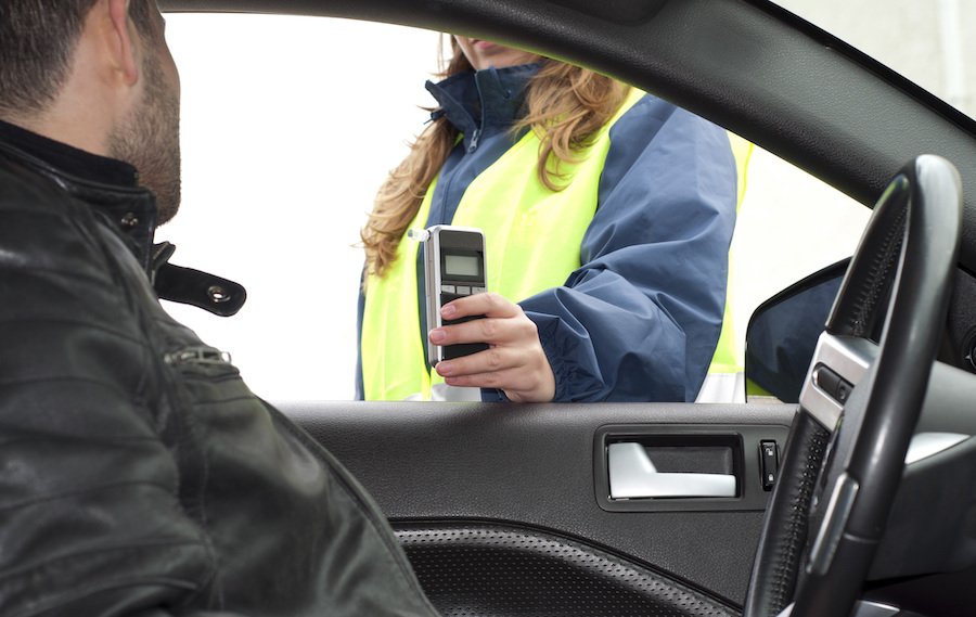 Police administering roadside breathalyzer test to DUI suspect behind the wheel