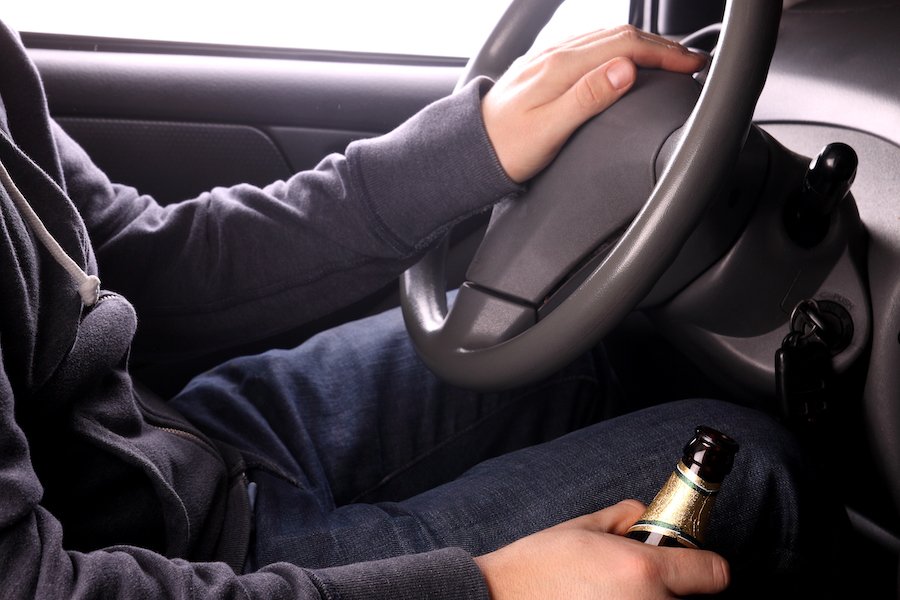 Driver with one hand on wheel and the other holding a beer