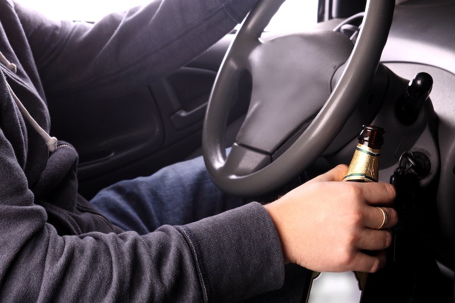 Driver with one hand on wheel and the other holding a beer