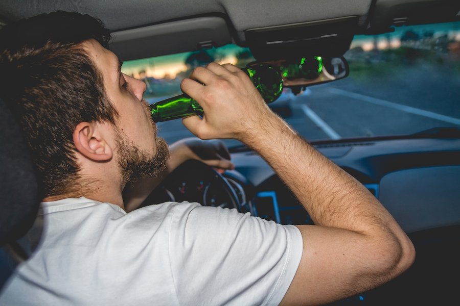Driver with one hand on wheel and the other holding a beer