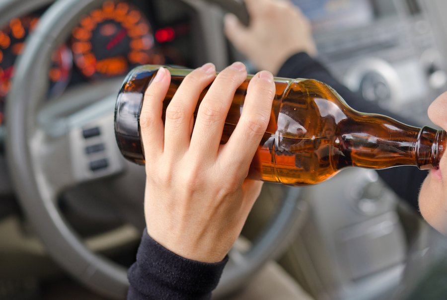 Driver with one hand on steering wheel and other on beer bottle