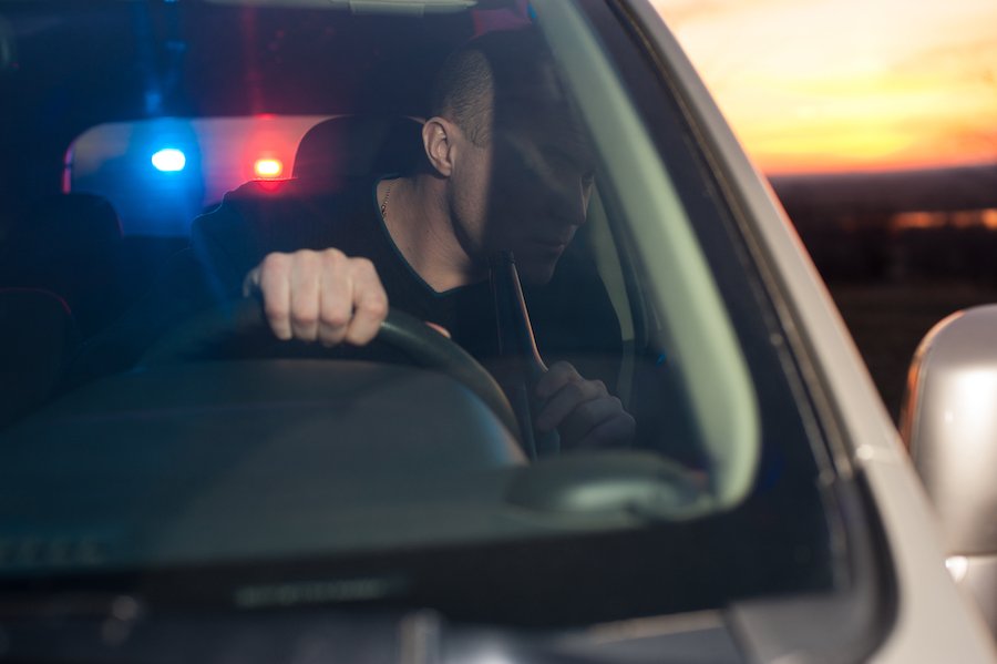 Un hombre detrás del volante bebiendo con la policía detrás de él