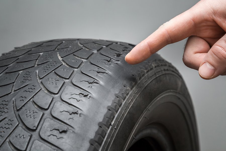 Man's hand finger pointing to the old, damaged and worn black tire tread. 