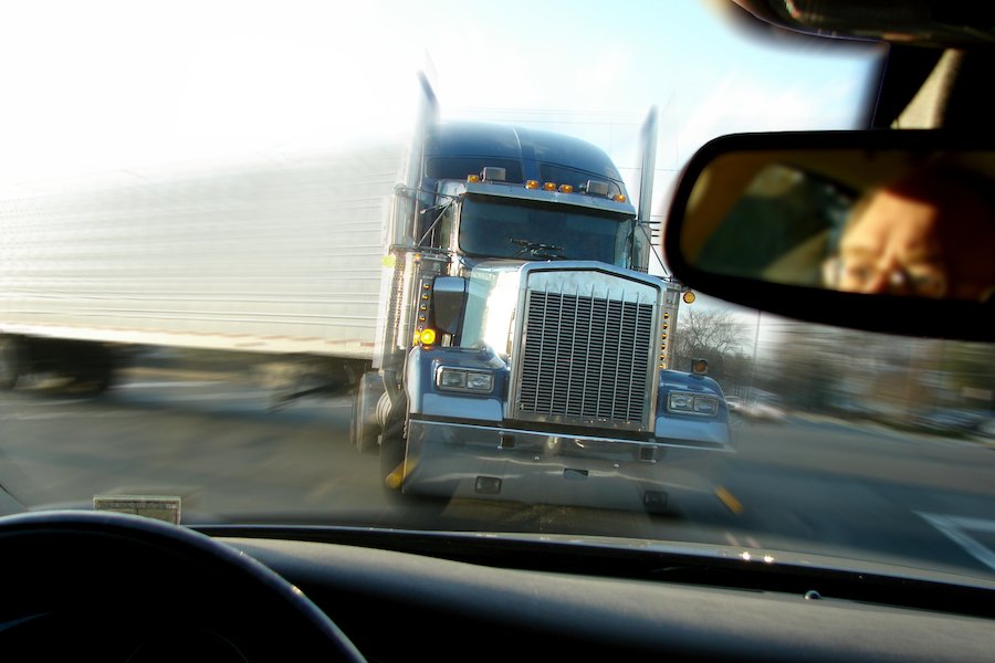 Close call imminent crash accident with a tractor trailer truck viewed from inside a passenger car with scared driver face in rear view mirror