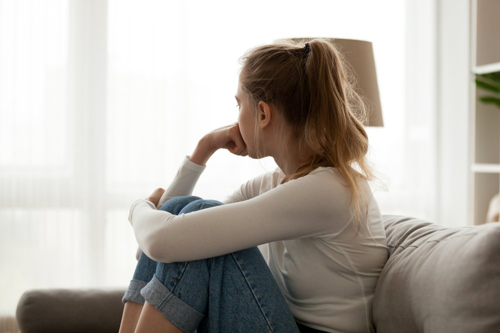 A young woman sadly looking outside a window.