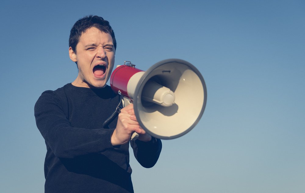 Hombre gritando en un megáfono como ejemplo de lo que podría ser conducta desordenada según la ley de Colorado 18-9-106 CRS