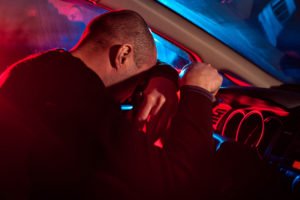 Conductor borracho inclinando la cabeza sobre el volante con luces de policía afuera