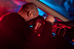 Conductor ebrio inclinando la cabeza sobre el volante con luces de la policía afuera