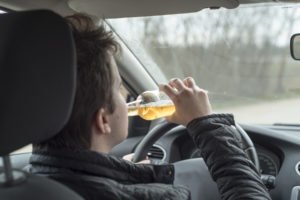 Hombre conduciendo mientras bebe cerveza: una 4ª DUI en California puede ser tratada como un delito.