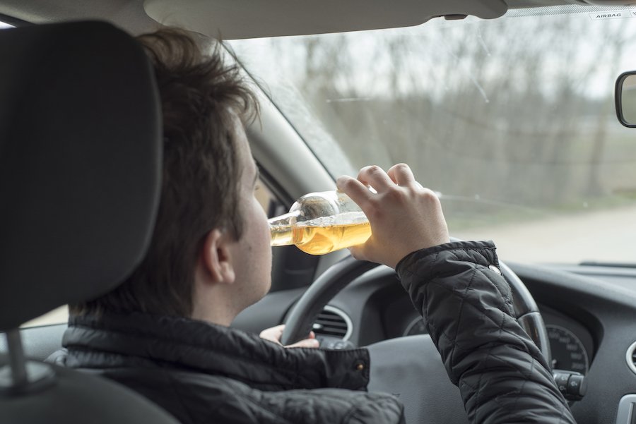 Young man driving his car while drinking alcohol