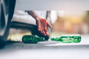 Bloody driver's hand hanging out of crashed car after dropping beer bottle