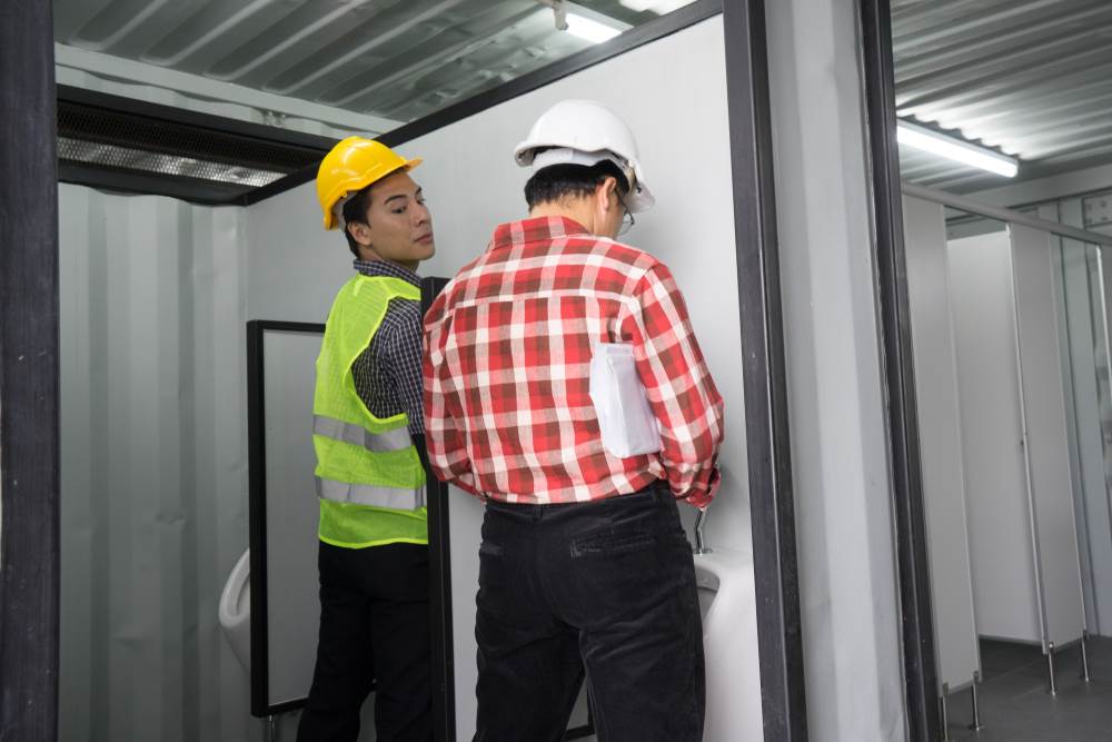 Un hombre mirando por encima del urinario en dirección al urinario de otro hombre.