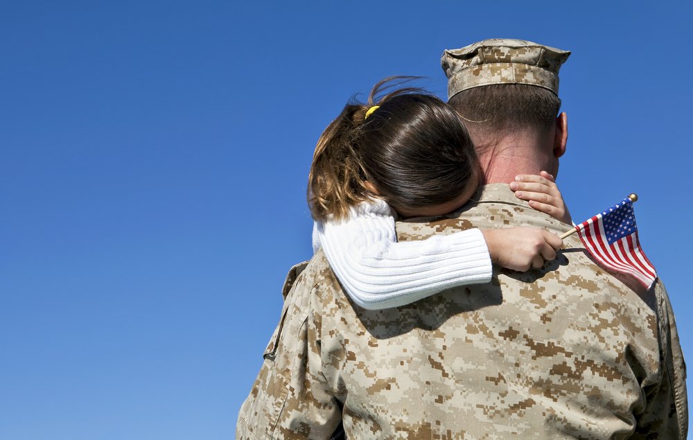 Niño abrazando a su padre que lleva un uniforme militar.