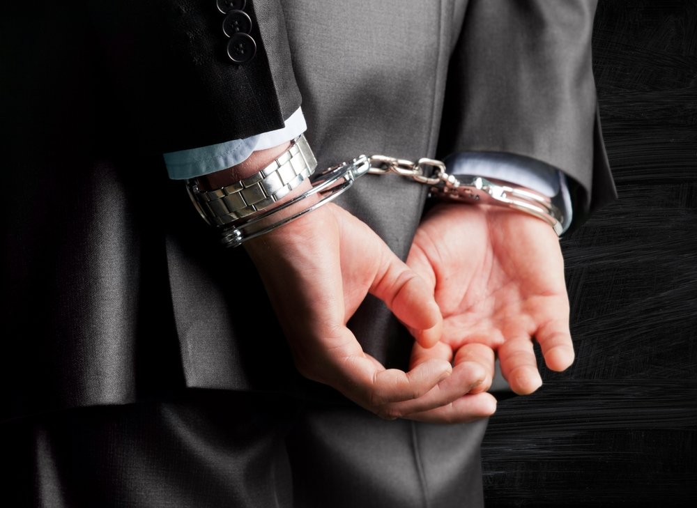 Suited man in handcuffs.