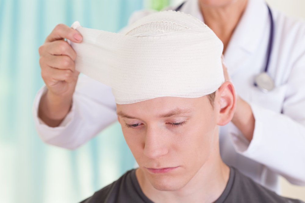 Un joven con su cabeza envuelta por un médico después de una lesión traumática.