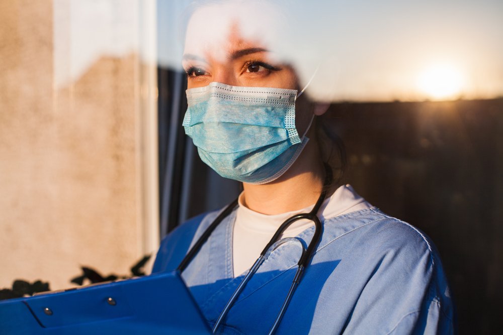 Nurse with a face mask looking outside a window.