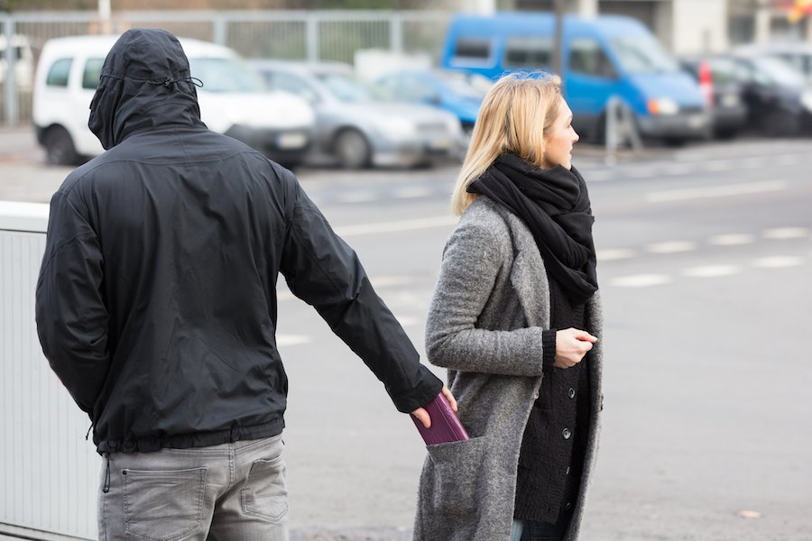 A man in a black hoodie pick-pocketing a mobile phone from a woman's coat pocket in a parking lot as an example of larceny from a person in Nevada