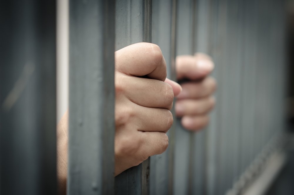Las manos de un prisionero agarrando las barras de una celda de prisión - la conducta sexual en una instalación correccional es un delito según el Código Revisado de Colorado 18-7-701