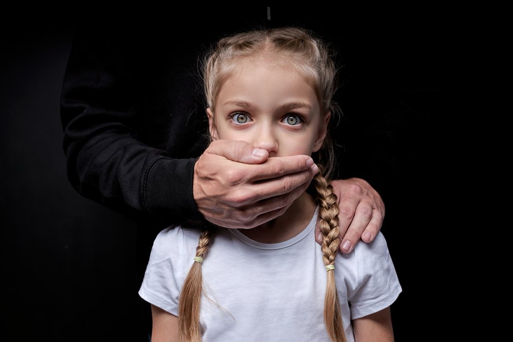 Adult hand covering the mouth of a young girl.