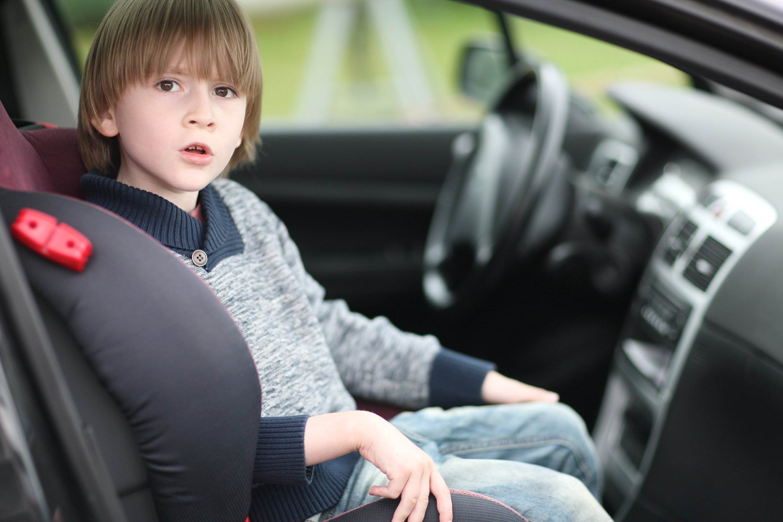 Un niño joven sentado en el asiento delantero del pasajero - La ley de asientos de seguridad para automóviles de California regula cómo deben asegurarse los niños pequeños mientras viajan en vehículos motorizados
