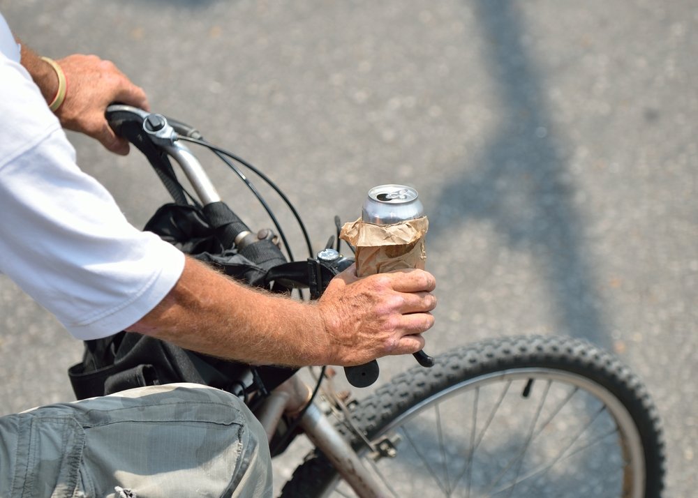 Man with an open beer can while riding a bike.