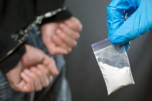 Picture of baggie of cocaine and handcuffed drug dealer, who faces an enhanced prison term under California Health & Safety Code 11370.4 HS