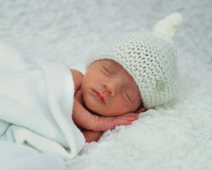 Preemie in a hat sleeping under a blanket
