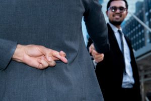 A non-lawyer shaking hands with a client while the non-lawyer crosses his fingers behind his back, indicating he is engaging in the unauthorized pratice of law in violation of BPC 6126 in California