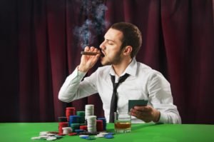 Hombre fumando puro en mesa de casino de cartas.