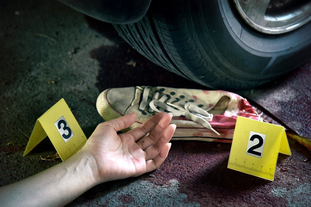A person's bloodied hand next to a vehicle tire.