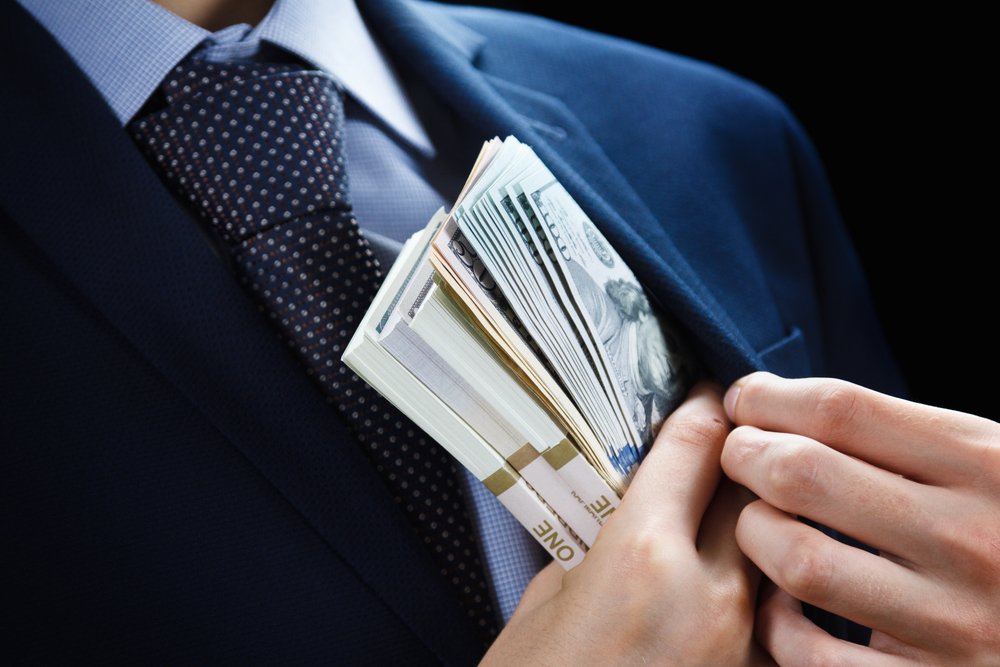 A businessperson putting a bundle of cash into his coat pocket.