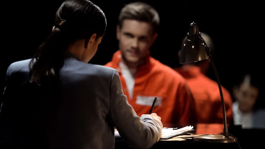 Un hombre en un mono de prisión naranja hablando con su abogado.