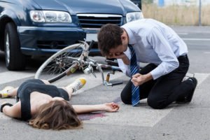 Automovilista inclinándose sobre la víctima de bicicleta que atropelló porque ella no miró antes de girar, lo cual es un homicidio excusable según el PC 195