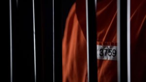 Man in orange jumpsuit behind prison bars serving felony sentence