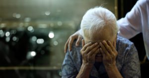 Elderly woman holding her head in her hands