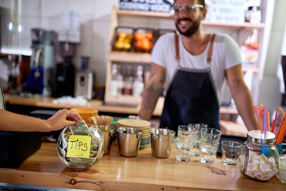 A barista smiling as he receives a tip.