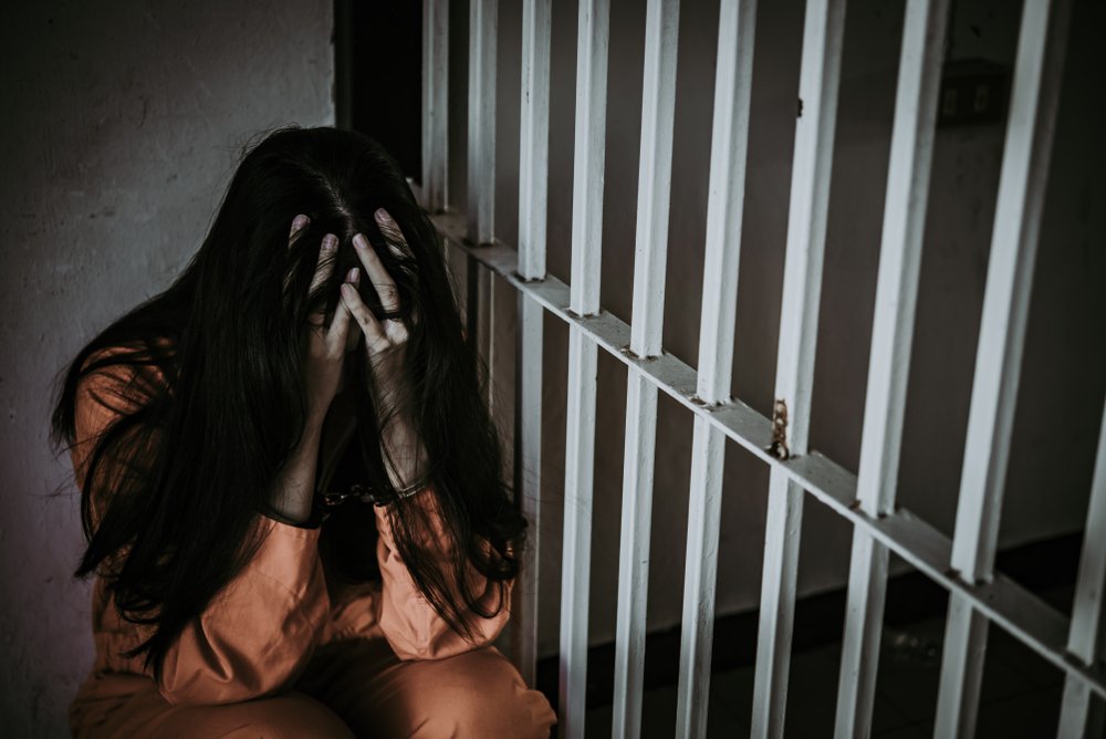 A withdrawn woman sitting with her head slumped in prison.