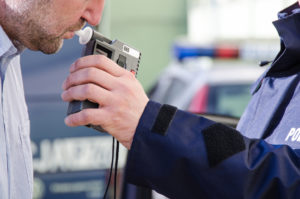 A driver blowing into a roadside breathalyzer after a DUI traffic stop
