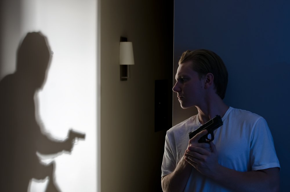 A man holding his gun as an armed burglar enters his house.