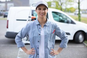 A smiling delivery driver in front of her delivery van.