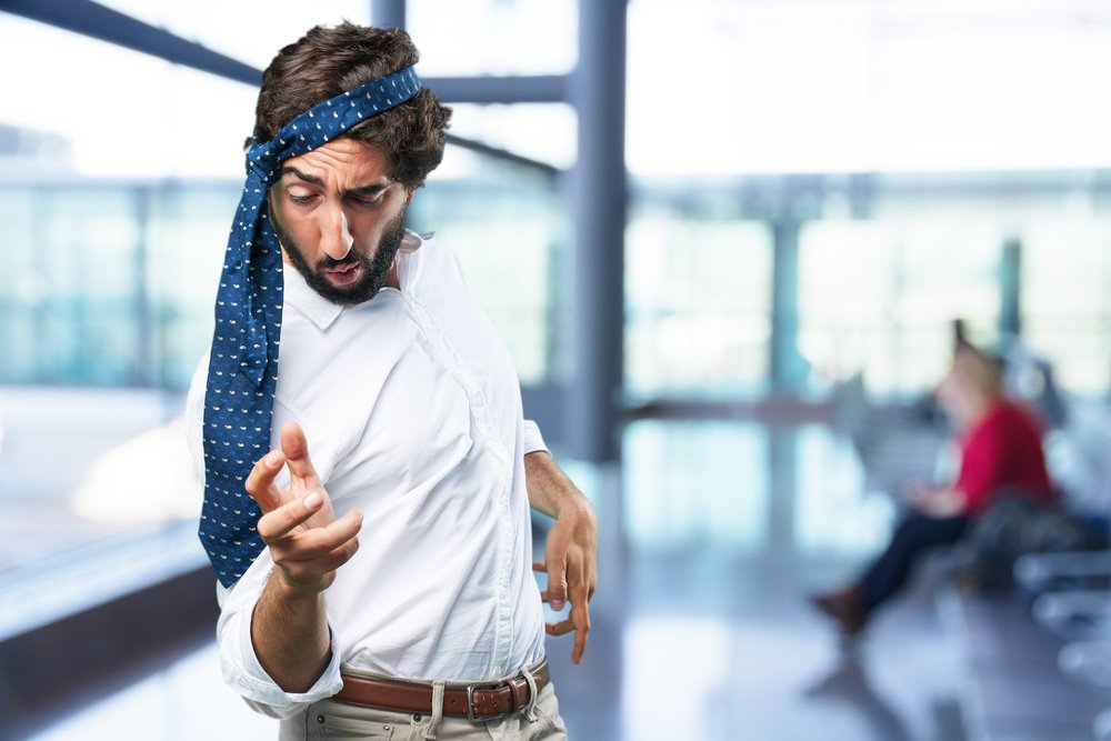 A man acting very drunk by tying his necktie around his head in public.