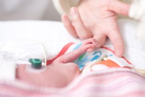 Adult hand holding hand of preemie baby in NICU