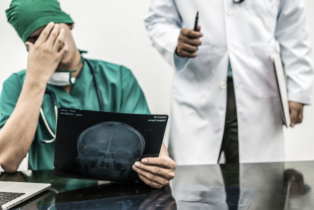 A doctor rubbing his forehead signifying the stress he might be feeling from a potential medical malpractice case.