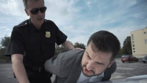 A police officer pushing down a man on top of a car.